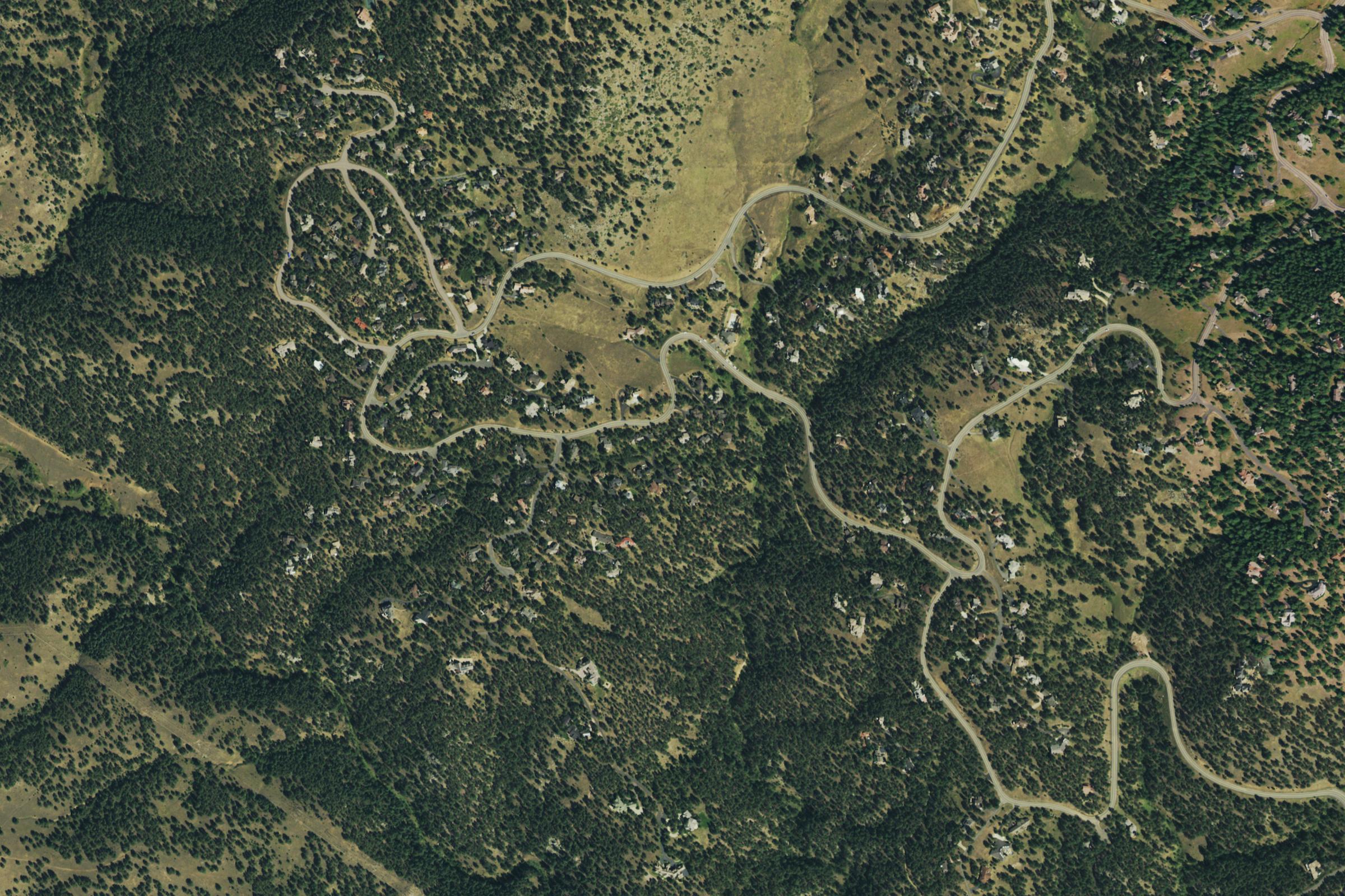 Aerial view of homes among wooded Colorado foothills and winding mountain roads